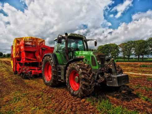 green tractor pulling red bin on field at daytime